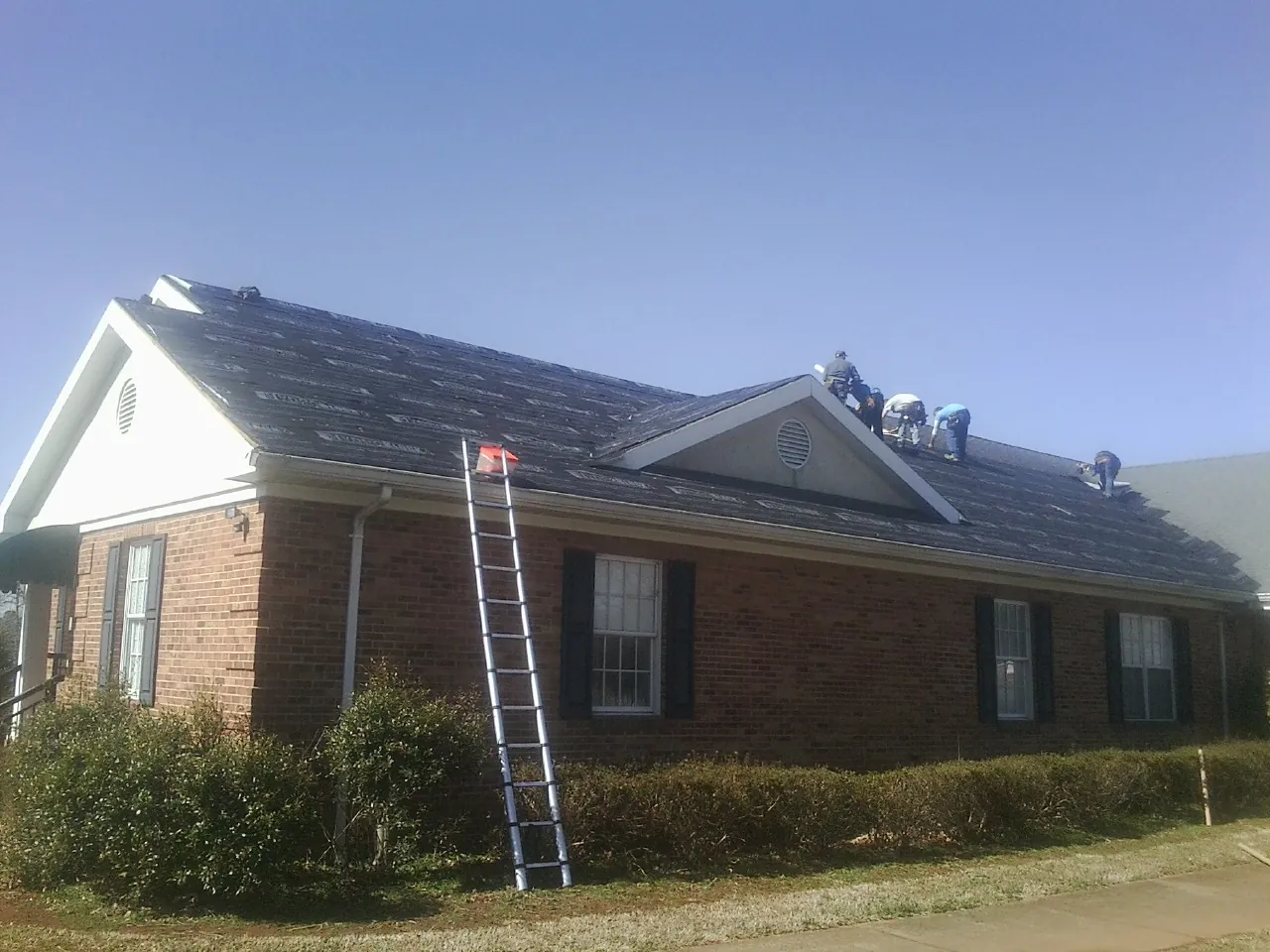 Crew tearing shingles off a brick ranch roof with a ladder set — Metal Roof Repair work by our crew in Troutdale