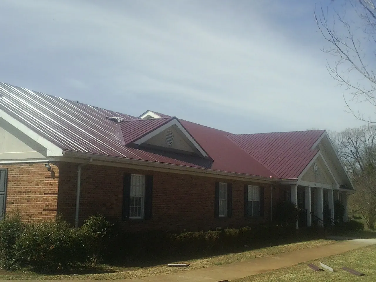 Red metal roof with gabled entries on a long brick building, from a Hail Damage Roof Repair job in Troutdale