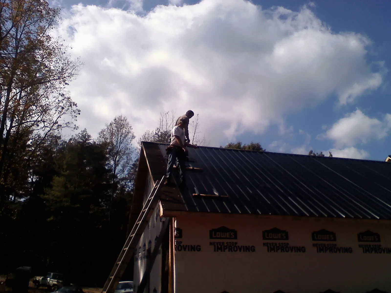 Roofer fastening dark metal panels high against a cloudy sky, from a Roof Inspection job in Troutdale