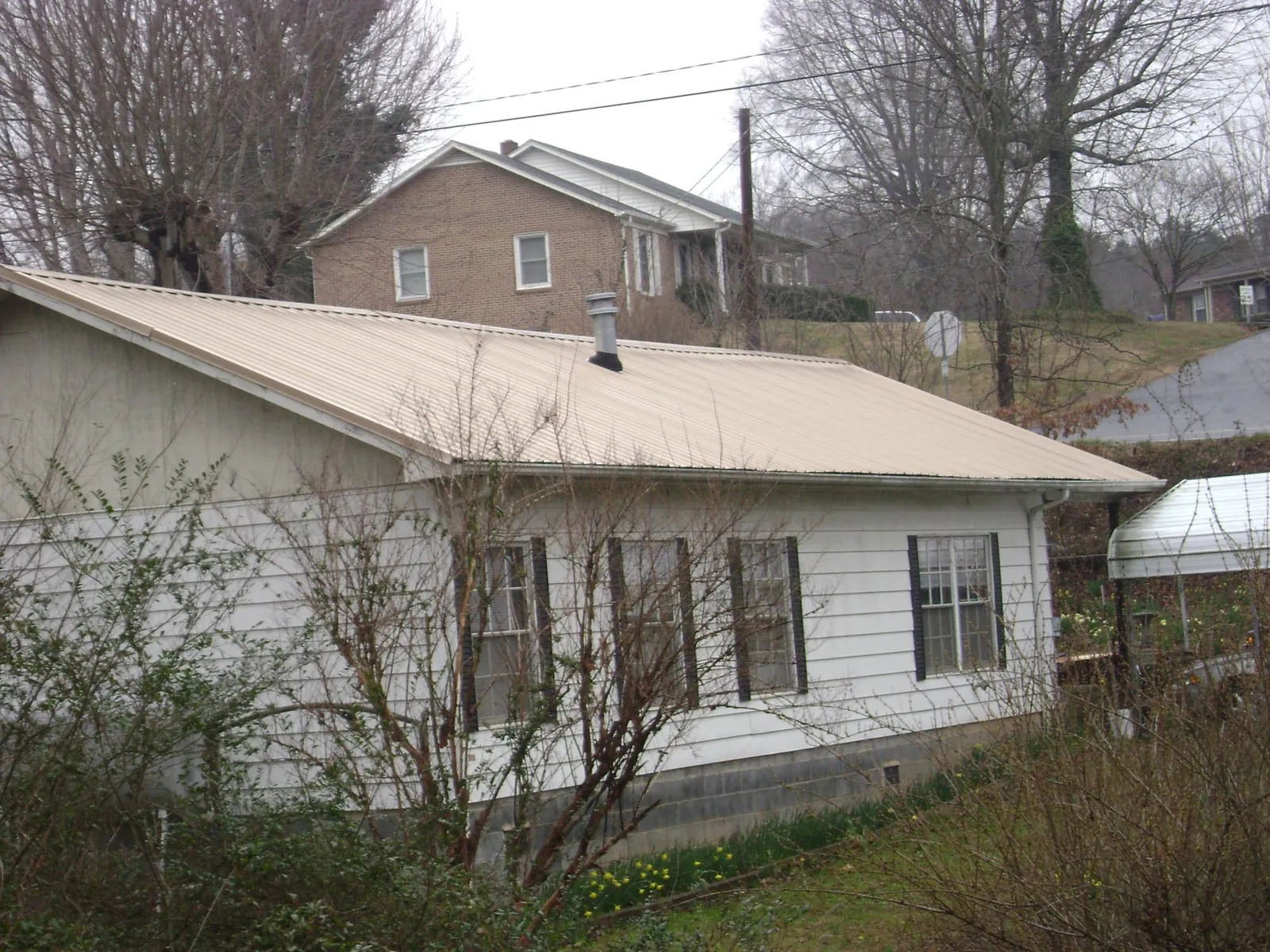 Tan metal roof on a white sided house set into a hillside — Commercial Roofing by Roofing Brothers in Troutdale